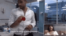 a man in a white shirt is holding a red heart in a room .