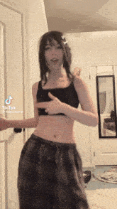 a woman in a black crop top and plaid pants is dancing in a bedroom .
