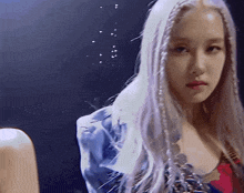 a woman with long white hair is wearing a blue jacket and red top .