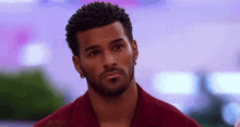 a man with a beard is wearing a red shirt and earrings and looking at the camera .