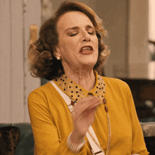 a woman wearing a yellow shirt and a gold collar is making a face
