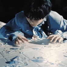 a man in a blue jacket is playing with broken glass on a tiled floor