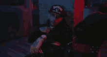 a man wearing a hat that says supreme is sitting in a dark room .