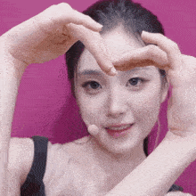 a woman making a heart with her hands on a pink background