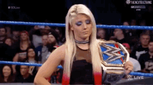 a woman in a black dress is holding a wrestling championship belt in a ring .