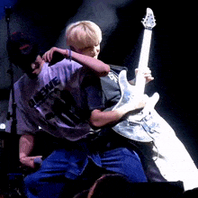 a man wearing a shirt that says ' leewe ' on it holds a guitar
