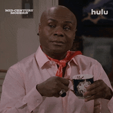 a man in a pink shirt is holding a cup of tea in front of a screen that says hulu