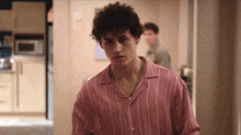 a man in a pink striped shirt is standing in a kitchen