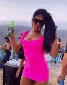 a woman in a pink dress is holding a bottle of heineken beer and smoking a cigarette .