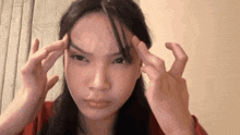 a woman is making a face with her hands on her forehead .