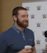 a man with a beard is talking into a microphone while holding a cup of coffee in his hand .