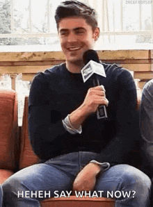 a man is sitting on a couch with a microphone in his hand and smiling .