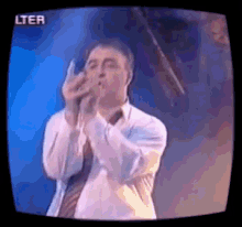 a man in a tie is singing into a microphone on a television screen .