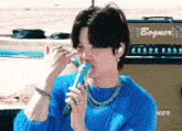 a man wearing a blue sweater is singing into a microphone with a bogner amplifier in the background