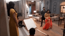 a man and a woman are standing in a living room . the woman is wearing a red saree .