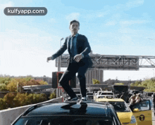 a man in a suit is standing on top of a car on a highway .
