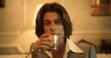 a man with long hair is drinking a glass of whiskey .