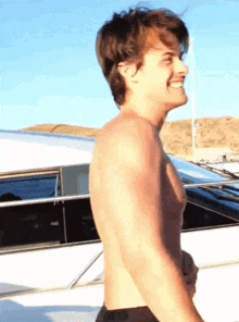 a shirtless man is standing in front of a boat .
