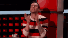 a man in a striped sweater is clapping his hands while sitting in front of a red chair .