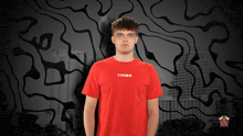 a man wearing a red tribe shirt stands in front of a black and white background