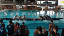 a group of people are watching a boat race in a swimming pool with a sign that says " leska " in the background