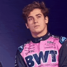 a young man wearing a pink bwt shirt is standing in front of a dark background .