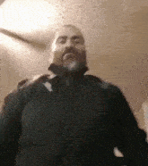 a man with a beard wearing a black jacket is standing in a room