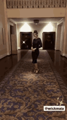 a woman in a black dress is standing in a hallway with the name erickmaia on the carpet