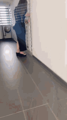 a woman is walking down a hallway with a fan in the background