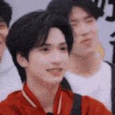 a young man in a red shirt is smiling and looking at the camera while standing in front of a group of people .