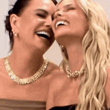 two women are laughing together and one has a necklace on her neck