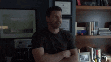 a man in a black shirt is standing with his arms crossed in front of a shelf .