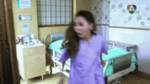 a girl in a purple dress is standing in a hospital room with a hospital bed .