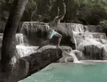 a man is jumping off a waterfall into a body of water .