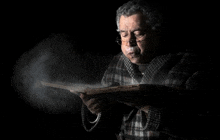 a man in a plaid robe is reading a book with smoke coming out of his mouth .