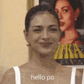 a woman in a white tank top says hello po in front of a poster of a woman .