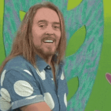 a man with long hair and a beard is smiling in front of a green background that says " i practise every day "