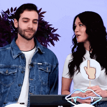 a man in a denim jacket stands next to a woman holding a finger up