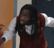 a man with dreadlocks is wearing a red vest and white shirt