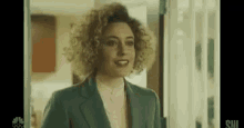 a woman with curly hair is wearing a green suit and standing in front of a window .