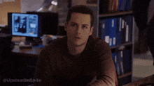 a man is sitting at a desk in front of a computer and looking at the camera .