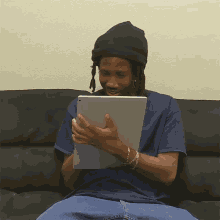 a man with dreadlocks is sitting on a couch holding a tablet
