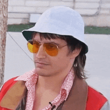 a man wearing a white hat and yellow sunglasses looks to his left