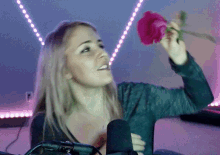 a woman in front of a microphone holds a pink rose