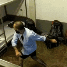 a man in a white shirt and tie is dancing in a room with bunk beds and backpacks