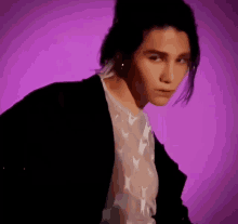 a man with long hair is standing in front of a purple background .