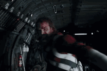 a man in a red jacket is holding another man in a helicopter .