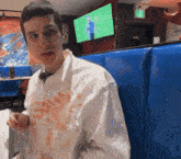 a man wearing a white shirt with a stain on it is sitting in a booth in front of a television