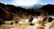 a man is riding a dirt bike on a dirt road with mountains in the background