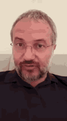 a man with glasses and a beard is sitting on a couch and making a funny face .